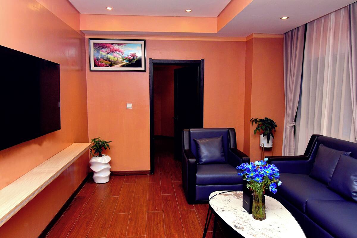 A modern living room with a flat-screen TV, a sofa, a chair, and a coffee table with a vase of flowers.