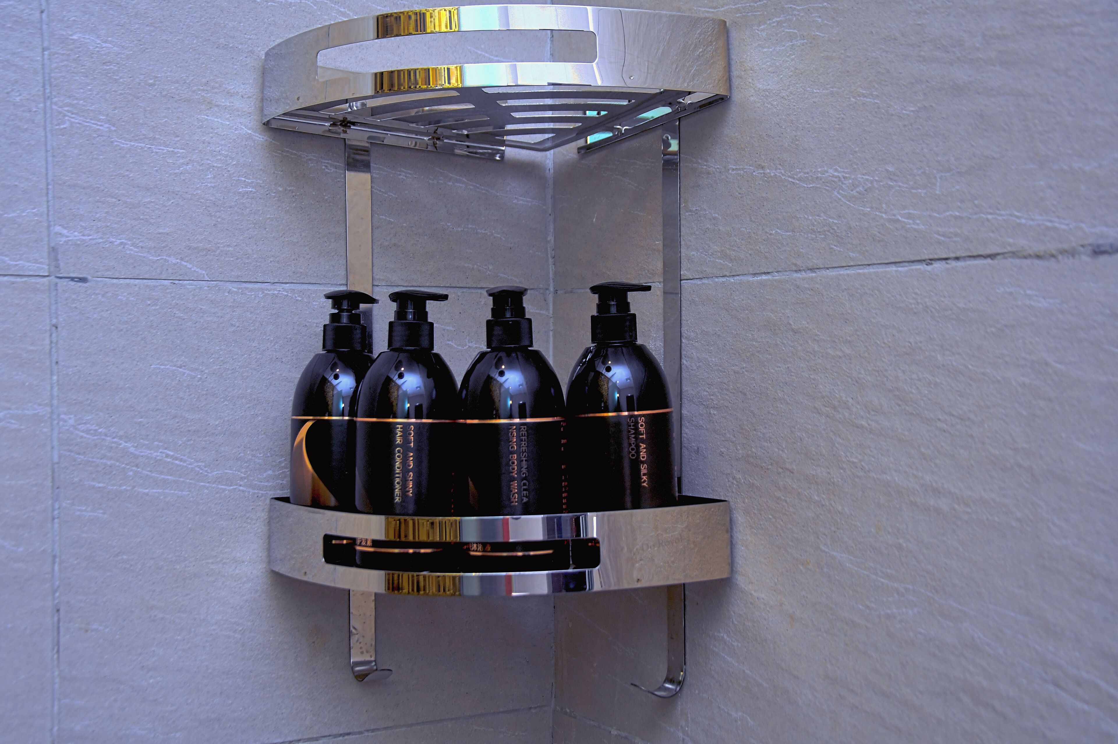 Casa de banho no canto com uma prateleira embutida que suporta quatro garrafas de shampoo e condicionador.