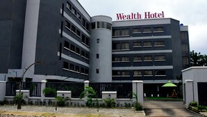 A modern building with a sign reading "Wealth Hotel." It features a curved facade, multiple windows, and a gated entrance.