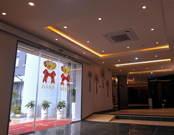A hotel lobby with a red carpet, potted plants, and a glass entrance with promotional posters. - Wealth Hotel (Lagos)