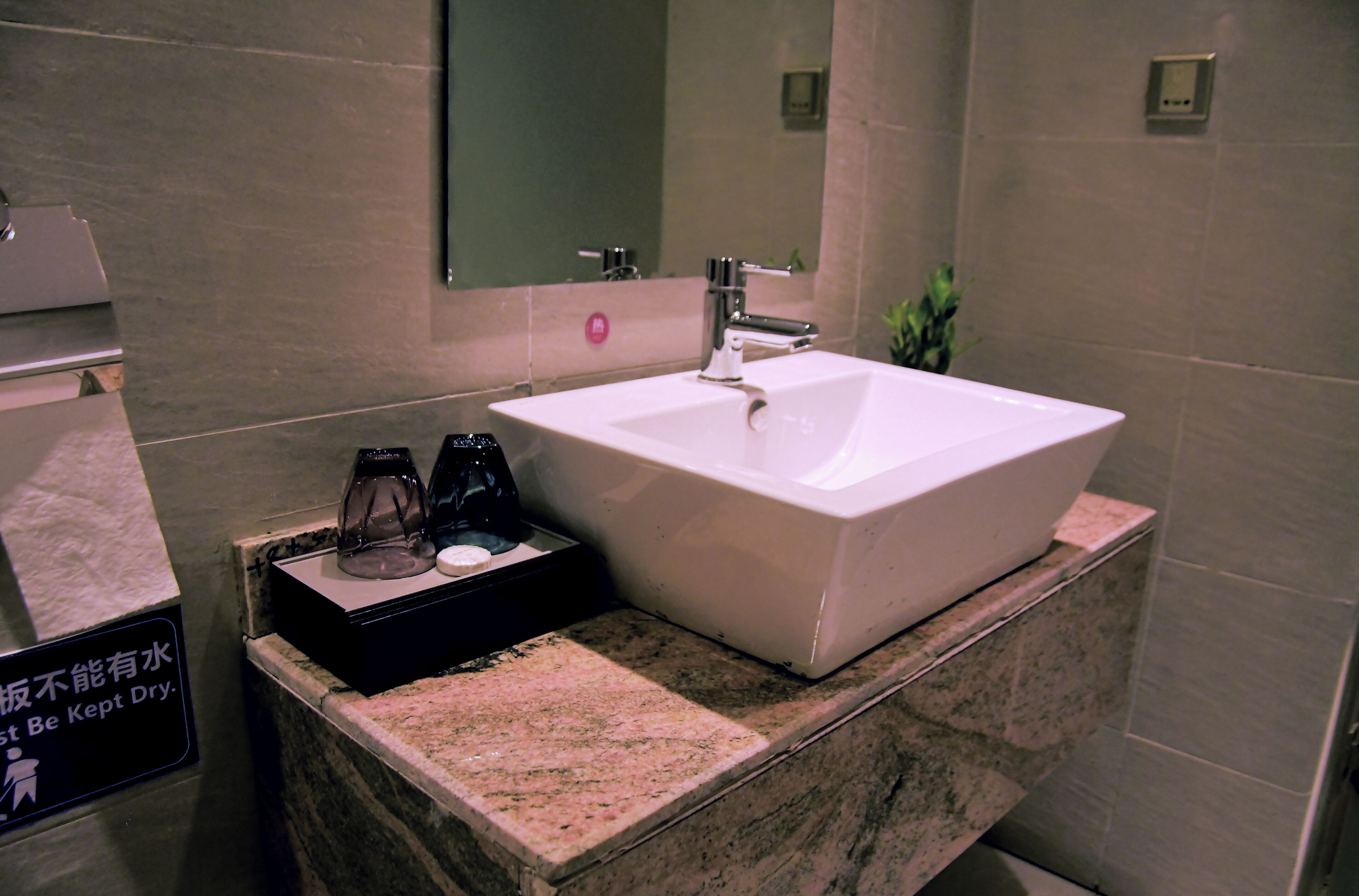 Un baño con un lavabo blanco, un espejo y un cartel que indica mantener el lavabo seco.