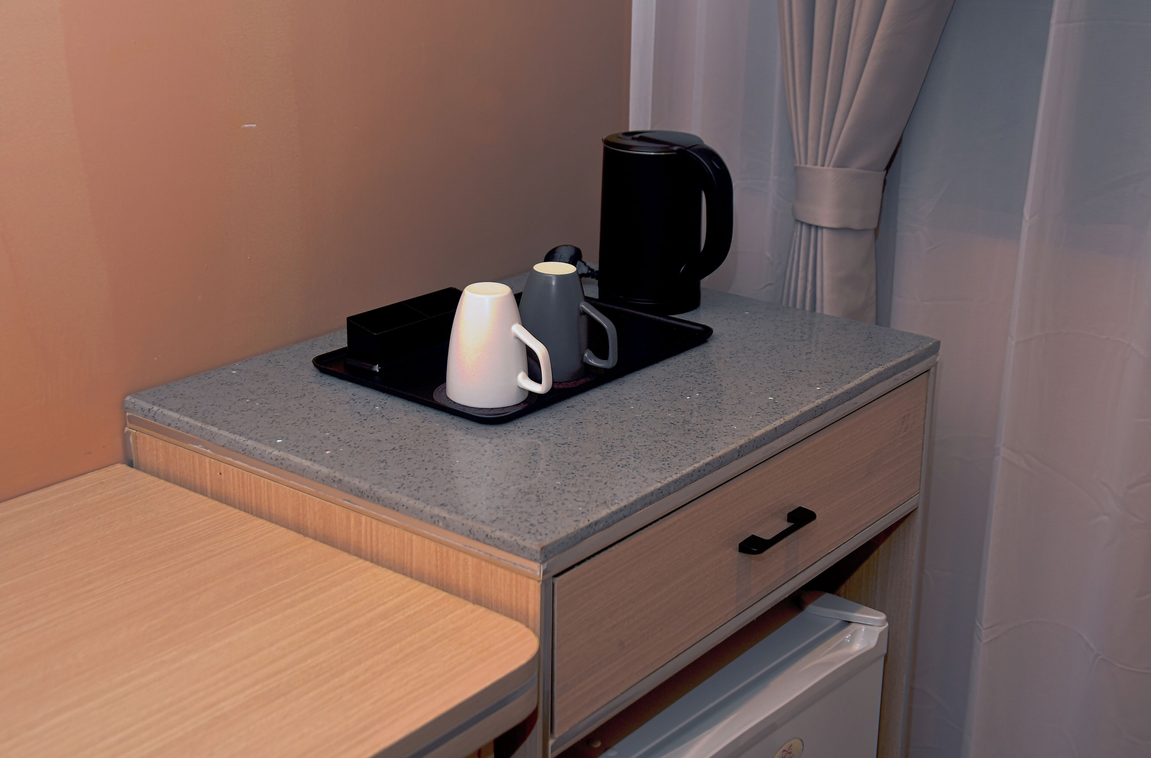A small kitchenette with a coffee maker, a mug, and a tray on a countertop.