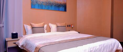 A neatly made bed with a white and beige bedspread, a nightstand with a tissue box, and a painting of a landscape on the wall.