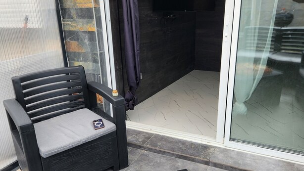 A patio with a black chair, a tray of food, and a glass door leading to a dark interior. - Quiet duplex with terrace 3min from Dijon + ring road. Ideal for professionals on the move (Longvic)