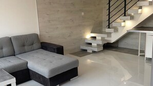 A modern living room with a grey sectional sofa, a white coffee table, and a staircase with built-in lighting. - Quiet duplex with terrace 3min from Dijon + ring road. Ideal for professionals on the move (Longvic)