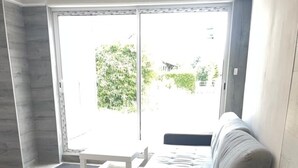 A modern living room with a grey sectional sofa, a small white side table, and a large sliding glass door leading to an outdoor area. - Quiet duplex with terrace 3min from Dijon + ring road. Ideal for professionals on the move (Longvic)