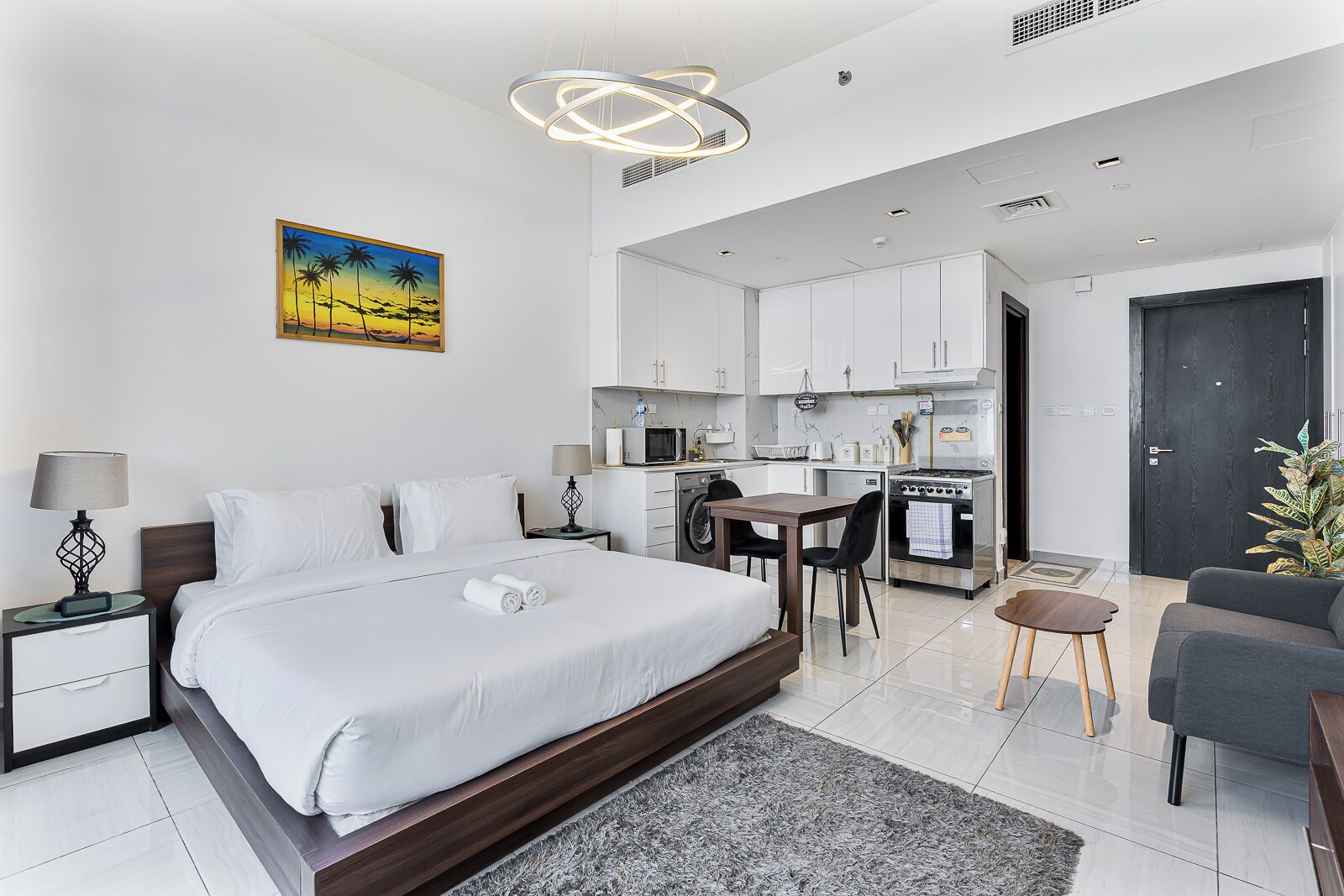 A modern hotel room with a large bed, a dining area, and a kitchenette.