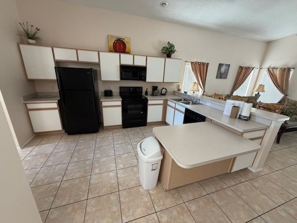 A compact kitchen with a refrigerator, microwave, stove, and sink. There is a small trash bin and a plant on the counter.