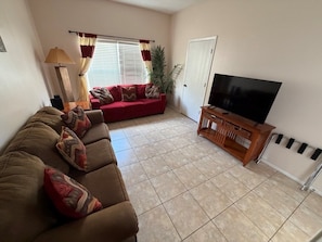 A living room with a sofa, a television, a lamp, and a window with curtains.