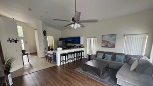 A spacious living room with a grey sectional sofa, a wooden coffee table, and a kitchen area in the background. - Lakeview Villa 5 Bedroom Home (Davenport)