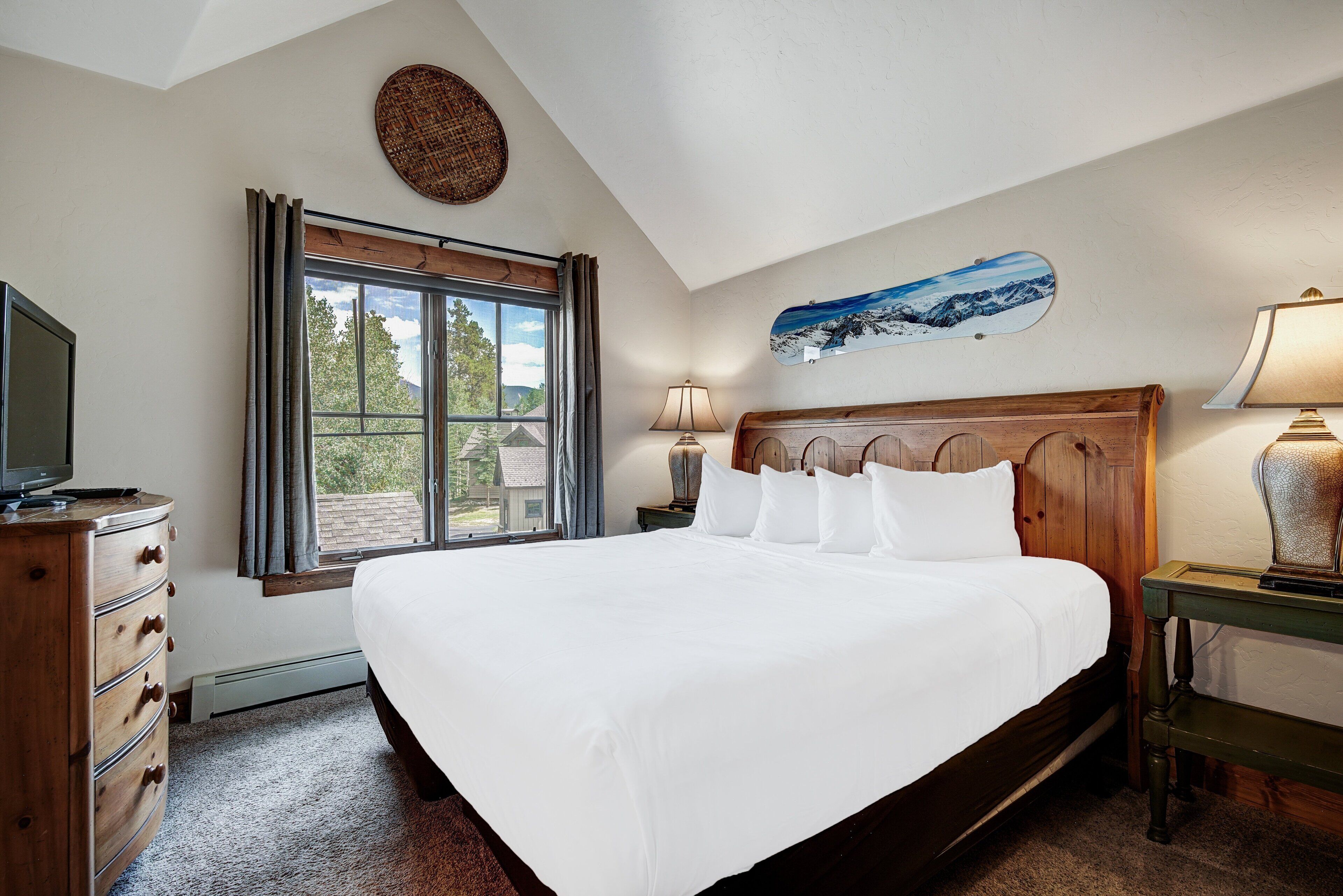 Une chambre à coucher avec un grand lit, une commode en bois, un téléviseur et une fenêtre avec des rideaux.