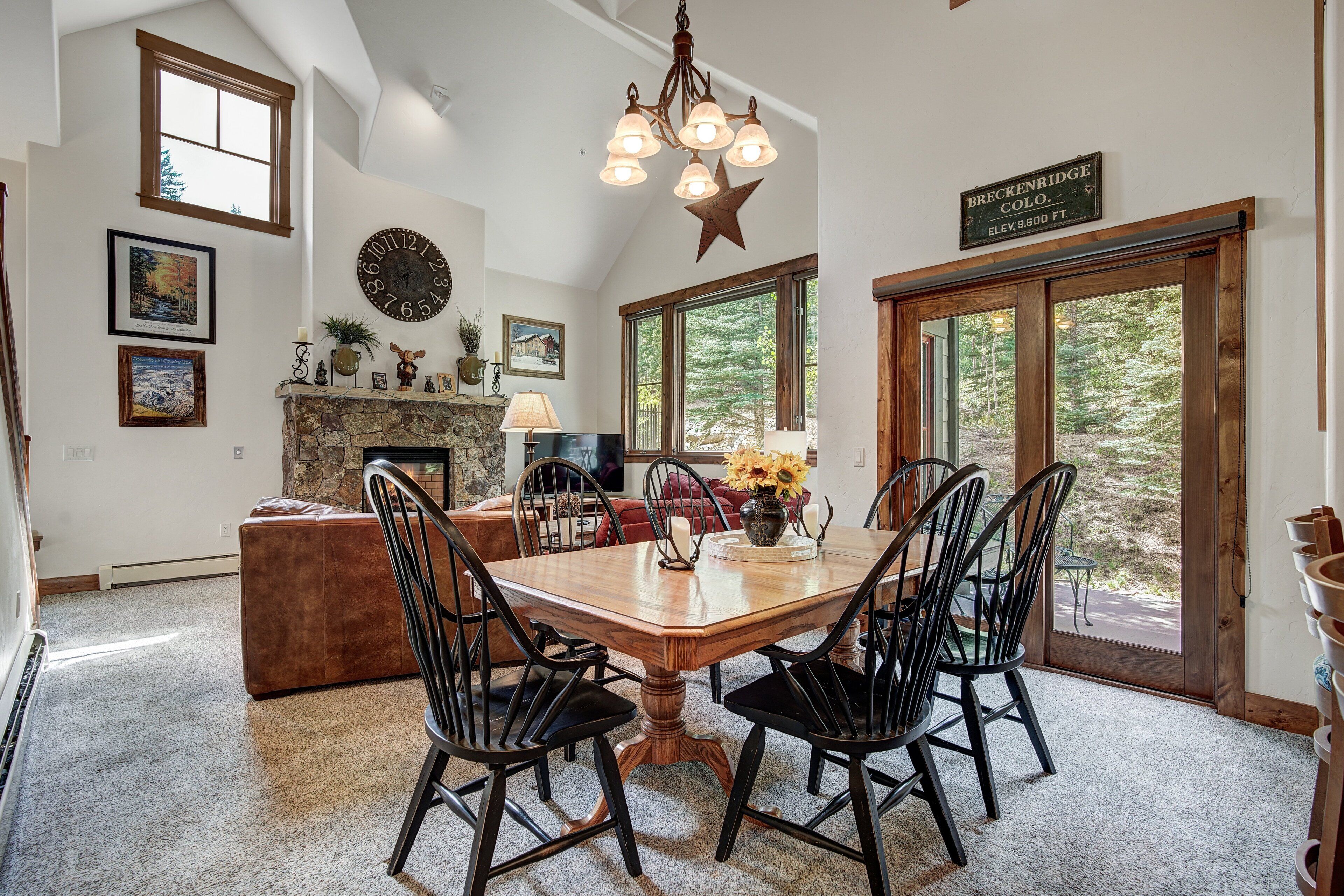 A dining area with a wooden table, black chairs, and a chandelier. There is a fireplace with a stone mantle, and a sign indicating the elevation of Breckenridge, CO.