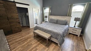 Une chambre à coucher avec un grand lit, un banc, une armoire et une fenêtre avec des rideaux.
