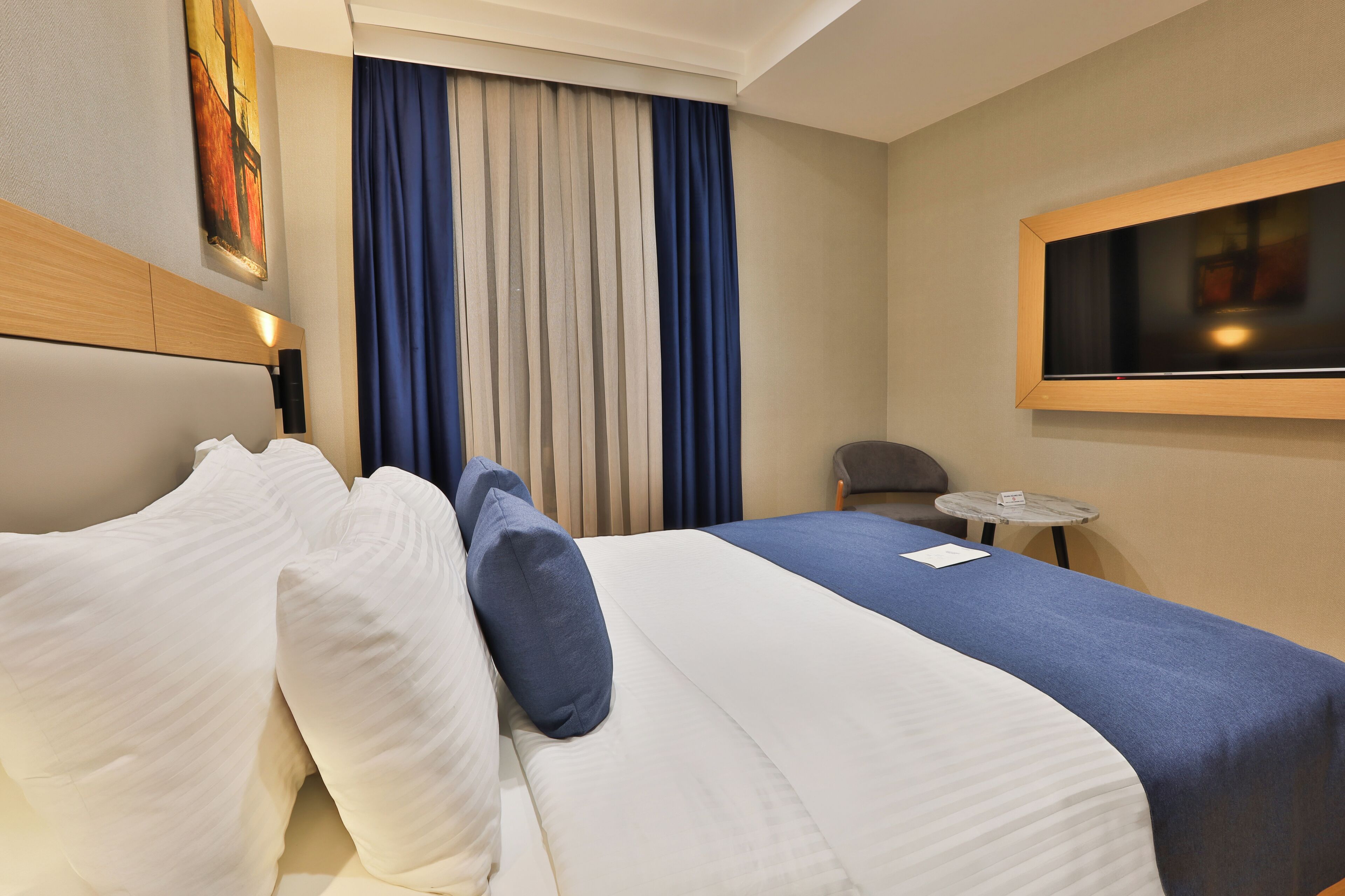 Une chambre d’hôtel avec un lit, une petite table, une chaise et un tableau au mur.