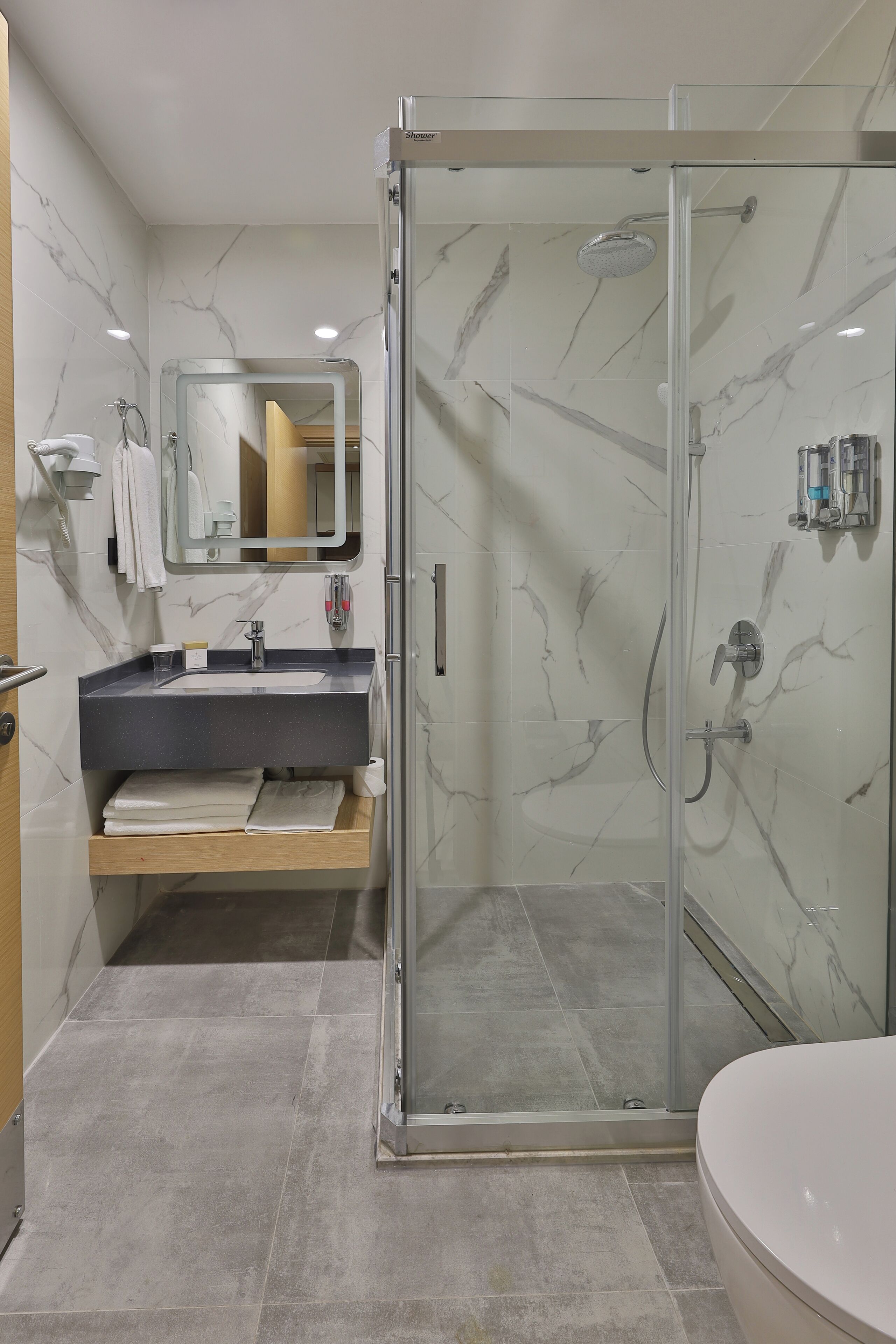 Een moderne badkamer met een douchecabine van glas, een wastafel met een marmeren blad en een grote spiegel.