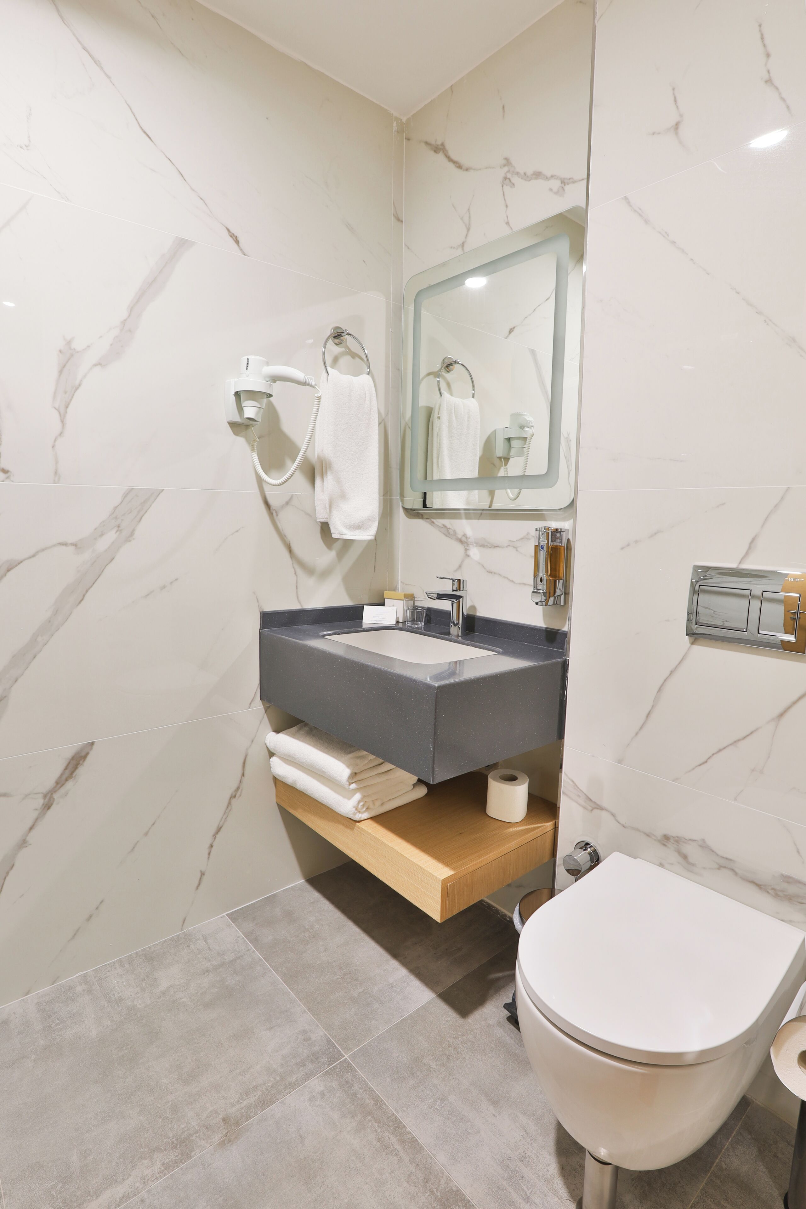 Une salle de bain moderne avec un mur en marbre, un lavabo encastré, des toilettes et un porte-serviettes.