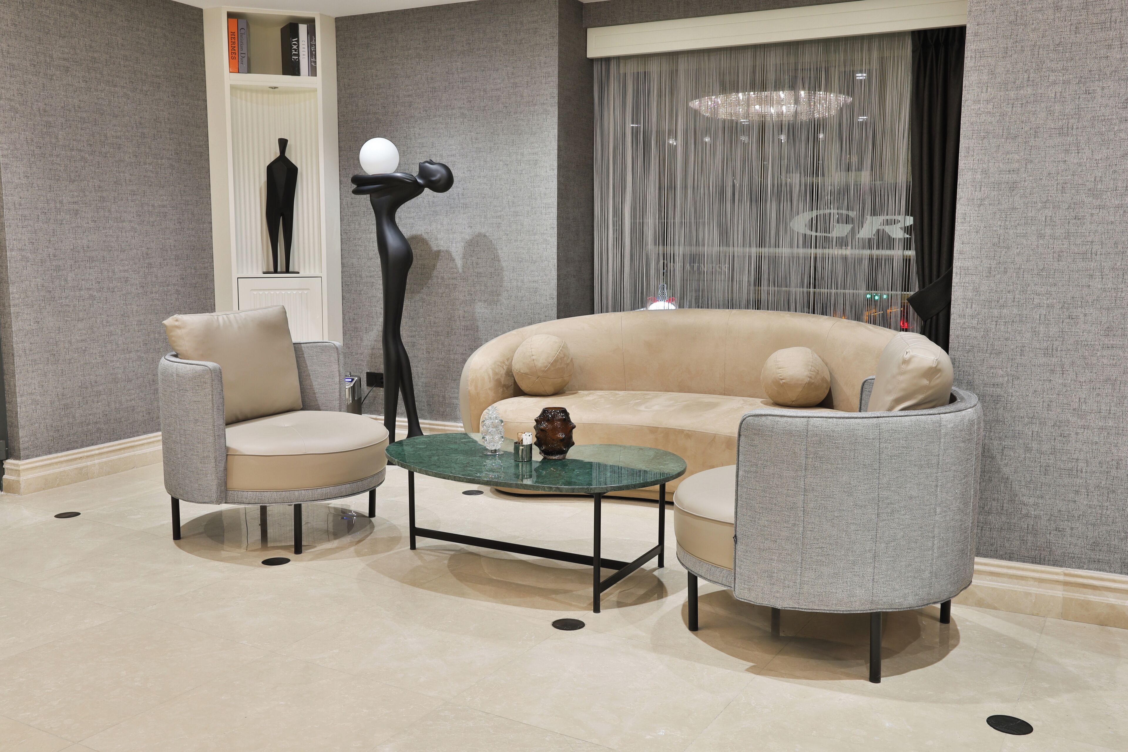 A modern living room with a beige sofa, two armchairs, and a glass coffee table.