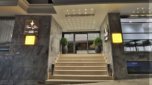 L’entrée d’un hôtel, avec un logo en forme d’étoile, des marches en marbre et des plantes en pot.