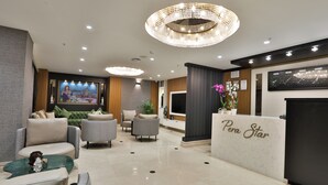 Un hall d’entrée moderne avec un comptoir de réception portant l’inscription « Pera Star », des fauteuils confortables, une grande fresque murale et un lustre décoratif.