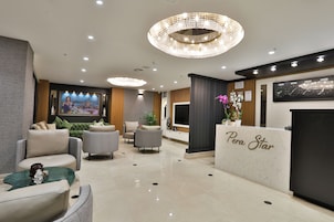 A modern lobby with a reception desk labeled "Pera Star," plush seating, a large mural, and a decorative chandelier.