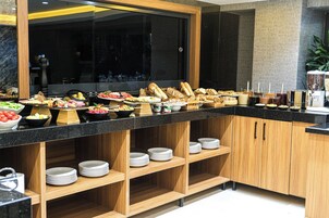 A buffet setup with various food items and beverages, wooden shelves with plates, and a modern kitchen area in the background.