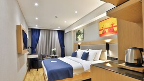 Une chambre d’hôtel moderne équipée d’un lit, d’une table de chevet et d’une bouilloire posée sur le comptoir.