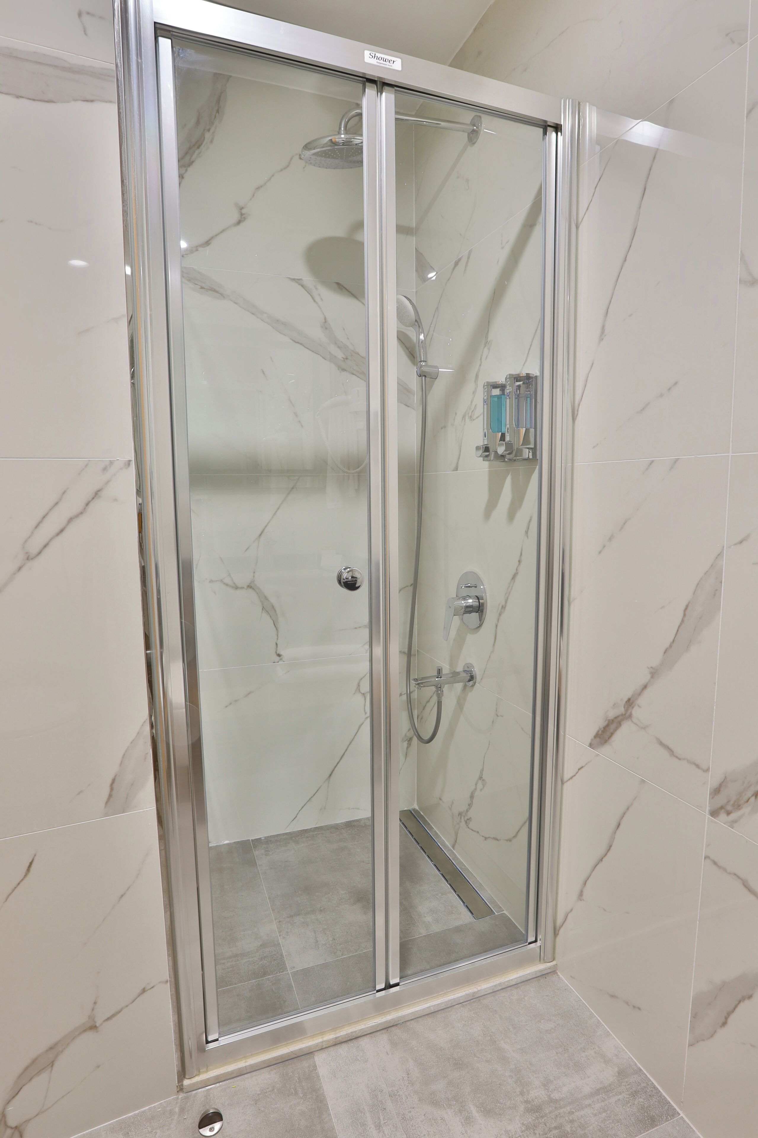 Ducha con mampara de vidrio, pared con azulejos de mármol, cabezal de ducha manual y control manual.