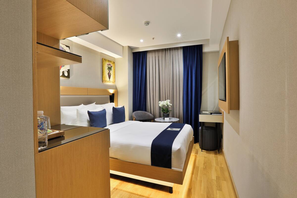 Habitación de hotel moderna con una cama grande, un escritorio, una silla, una mesita con un florero y un televisor.