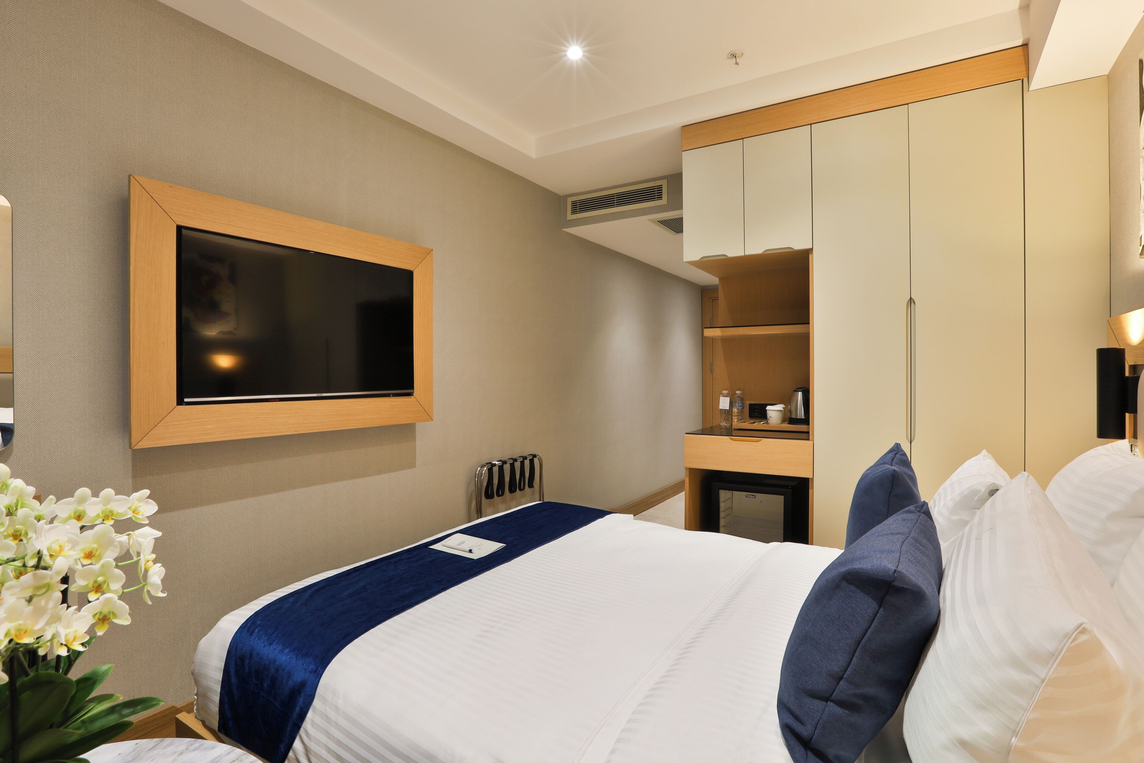 A hotel room with a bed, a TV mounted on the wall, a mirror, and a wardrobe.