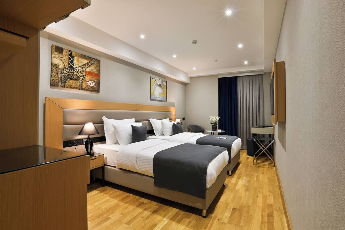 Una habitación de hotel con dos camas, un escritorio, una lámpara y obras de arte en las paredes.