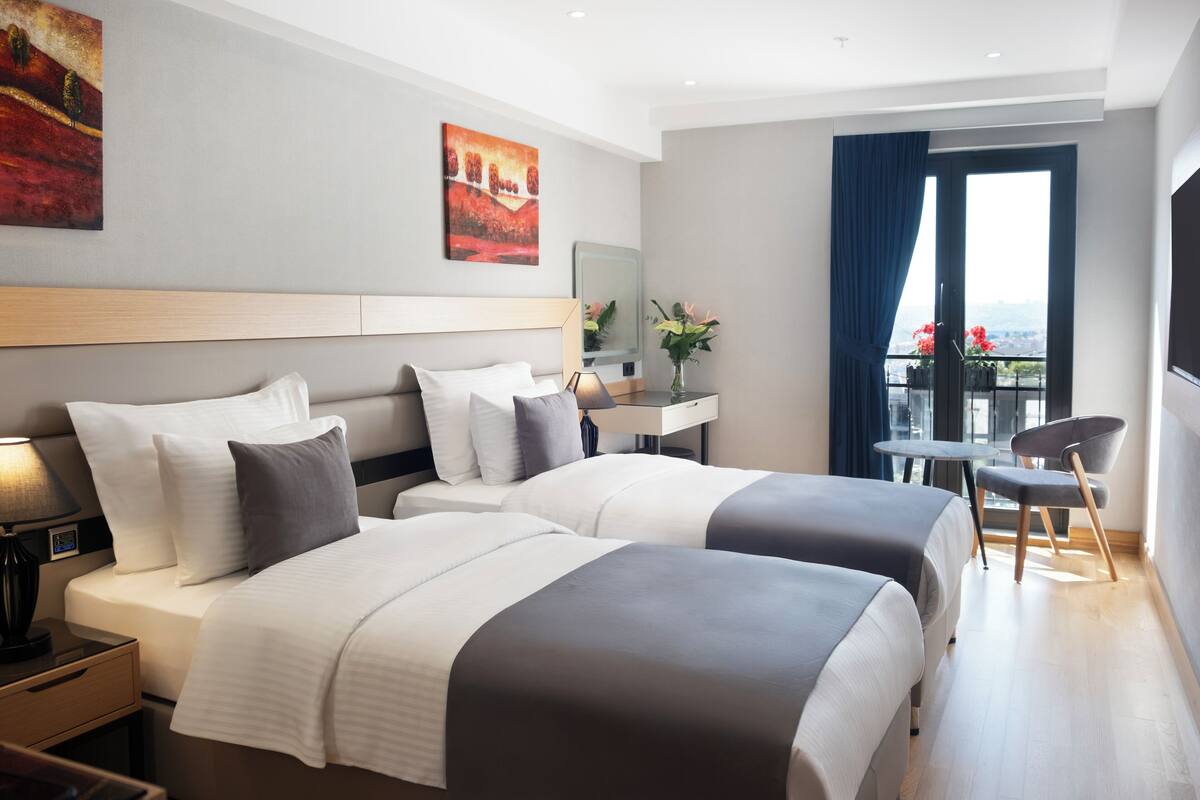 Habitación de hotel con dos camas, un escritorio, una silla y un balcón con vistas.
