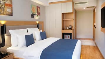 A modern hotel room with a large bed, a bedside table with a phone, a small seating area with a table and chairs, and a TV on the wall.