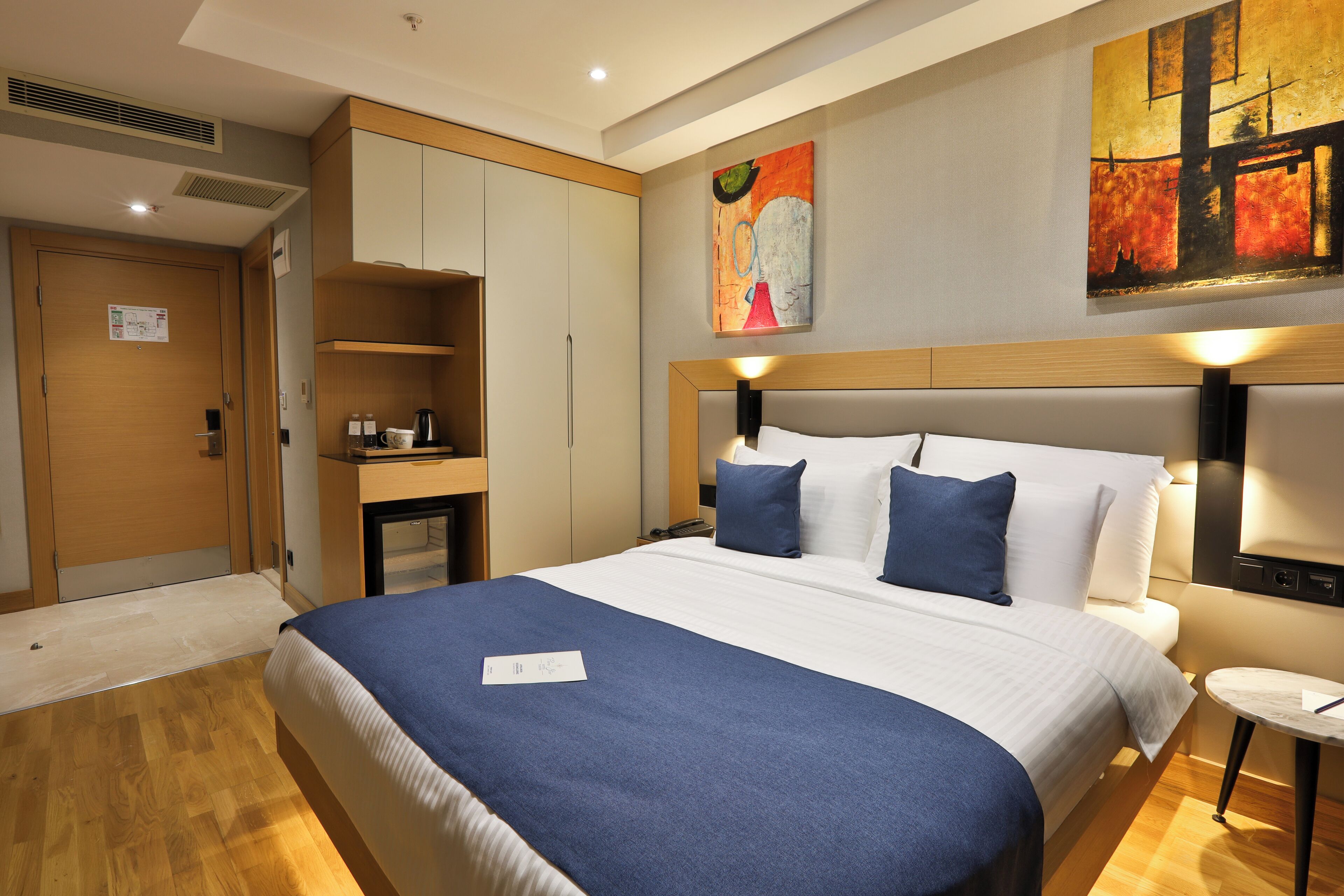 A hotel room with a large bed, a desk with a chair, a small table, and a painting on the wall.
