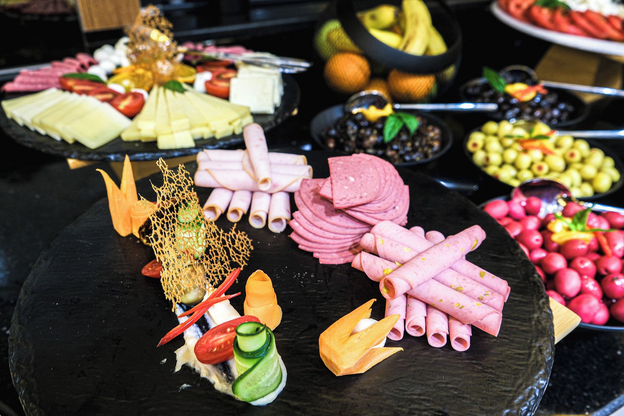 A variety of food items including cheese, meats, and fruits arranged on a black platter.