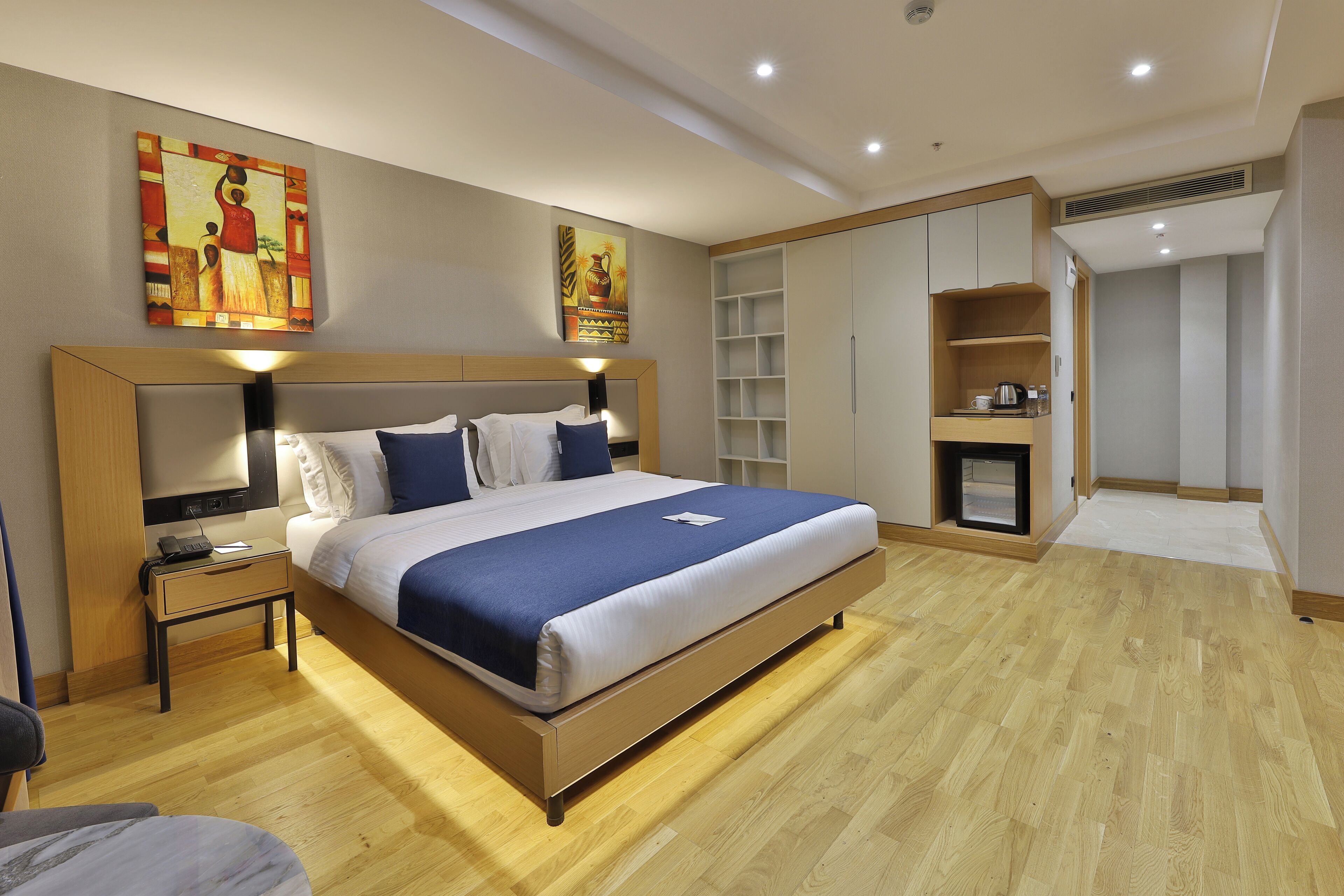 A modern hotel room with a large bed, bedside tables, a wardrobe, and artwork on the walls.