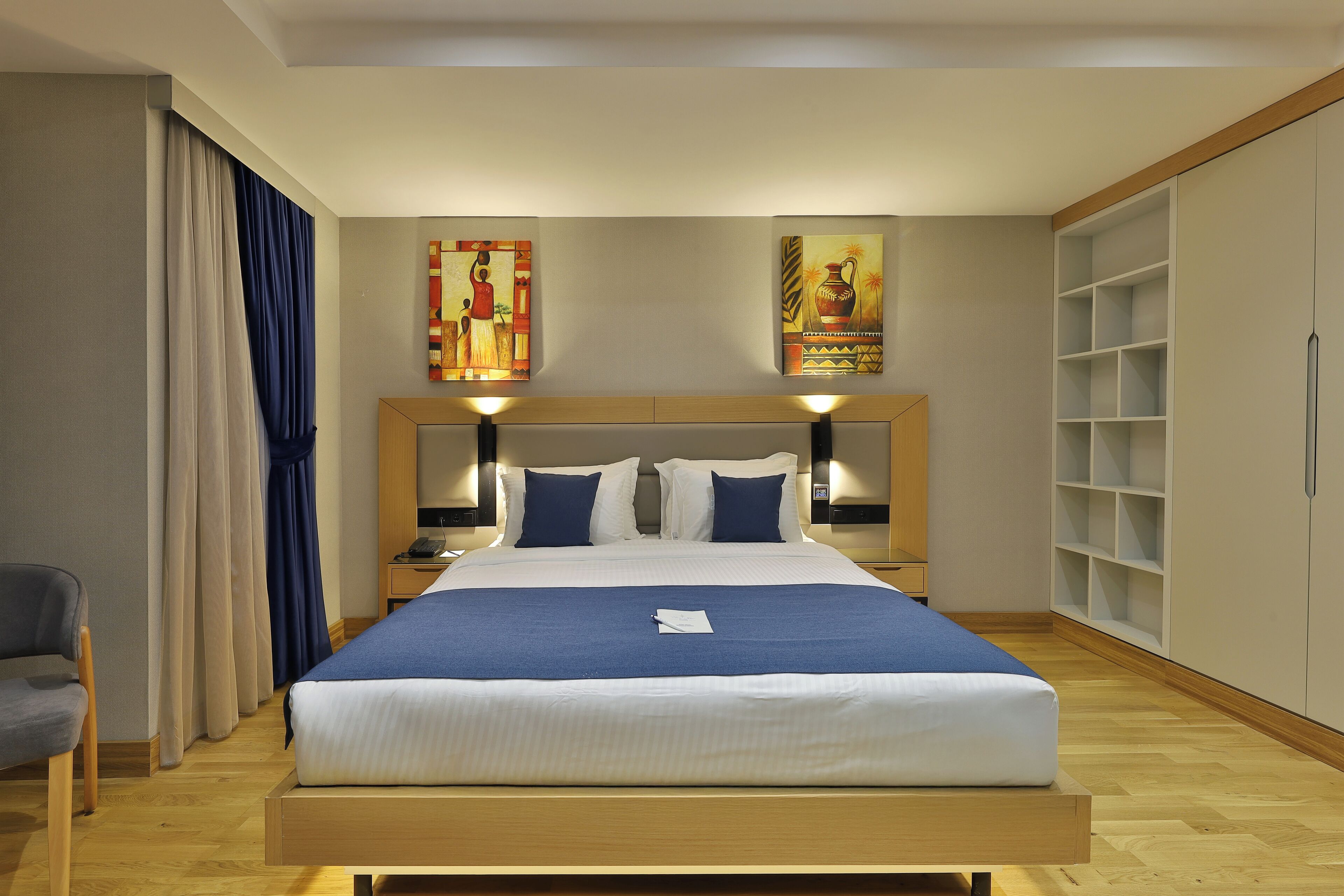 A neatly made bed with a blue blanket, a wooden headboard, and two wall-mounted lamps.