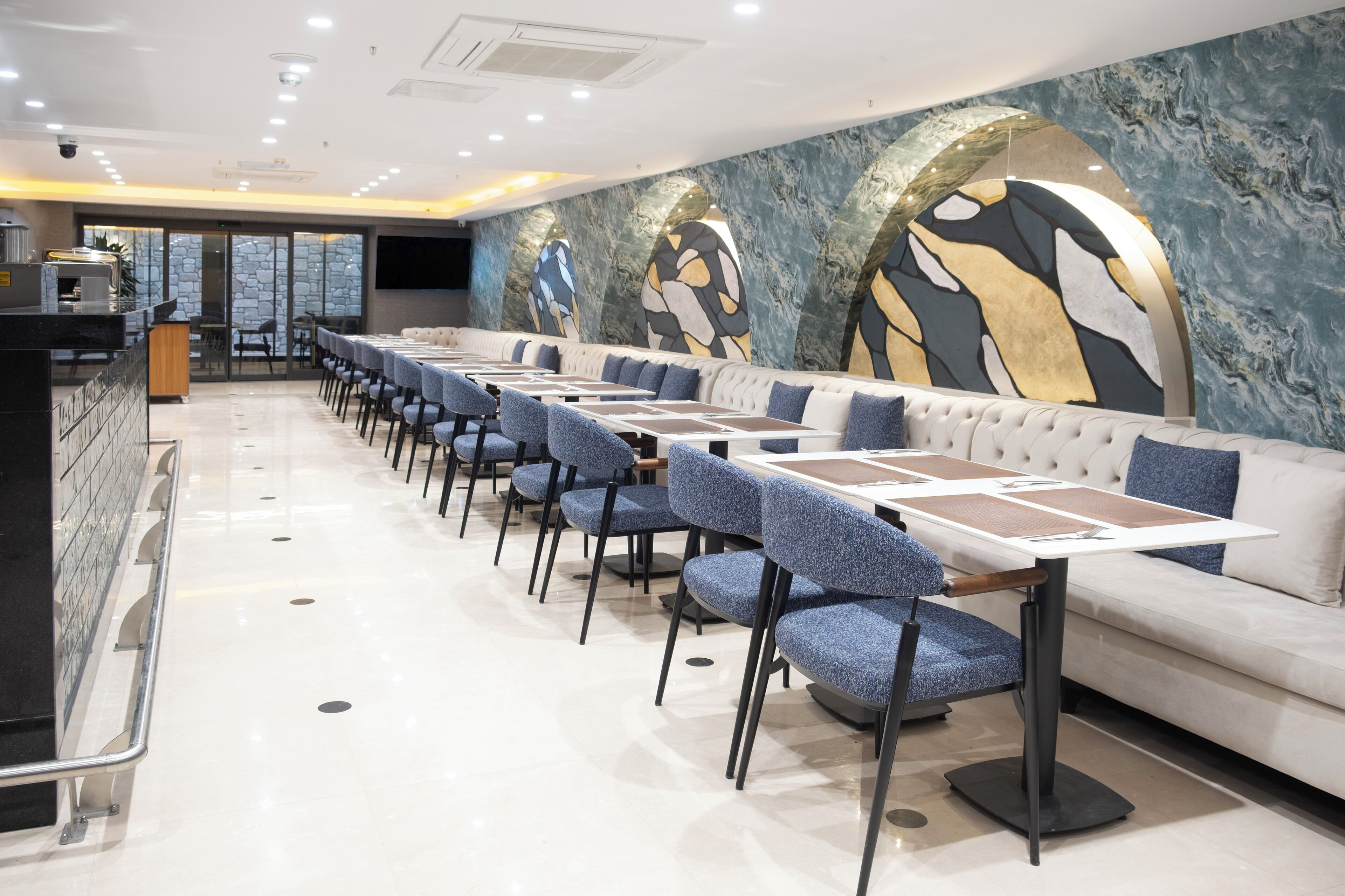 A modern restaurant with a long counter, blue upholstered chairs, and a white sofa.