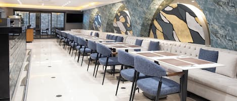Un restaurante moderno con una barra alargada, sillas tapizadas en azul y un sofá blanco.