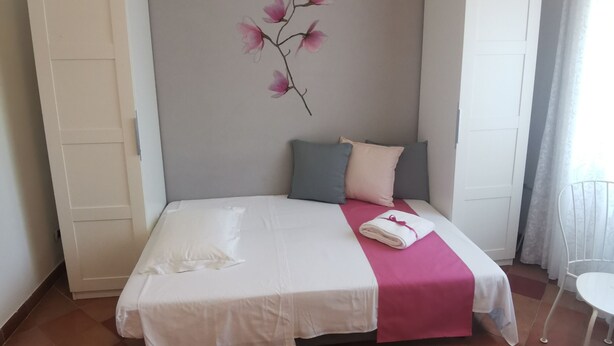 Un dormitorio ordenado con cama, almohadas, una toalla doblada, un adorno floral en la pared y un armario blanco.