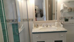 Un baño con ducha, lavabo con espejo y tocador con armarios.
