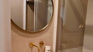 Une salle de bain avec un lavabo blanc, des robinetteries dorées, un miroir rond et une cabine de douche en verre.