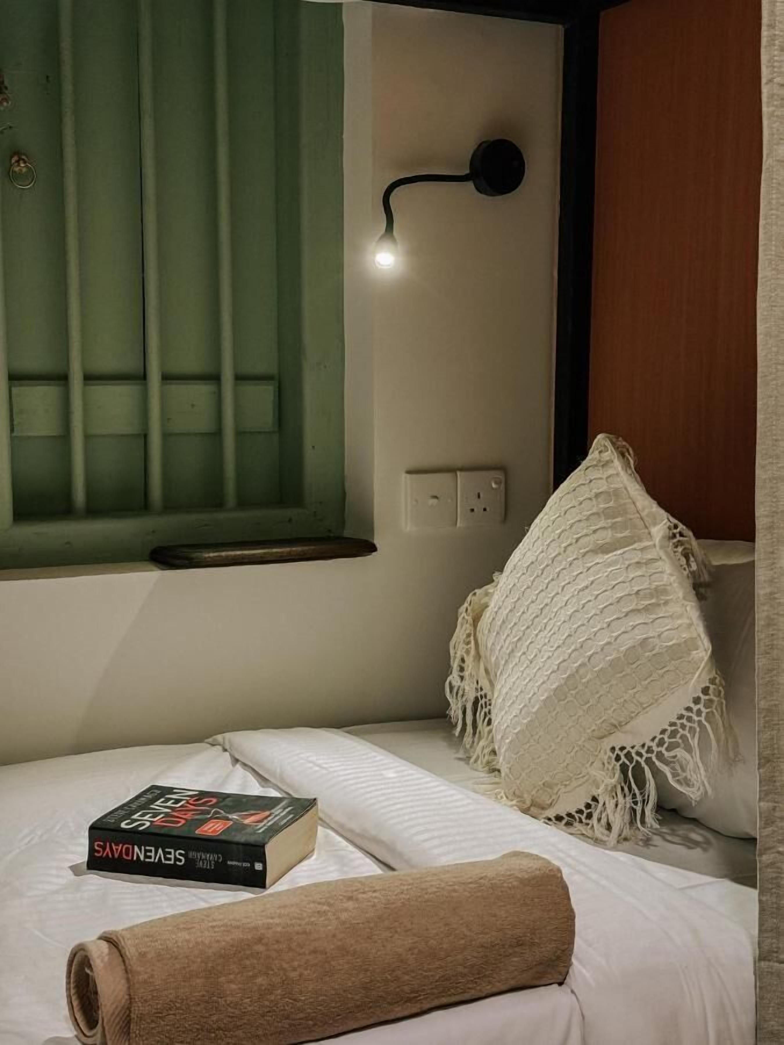 Una cama bien tendida con una toalla enrollada, un libro y un plaid con textura.