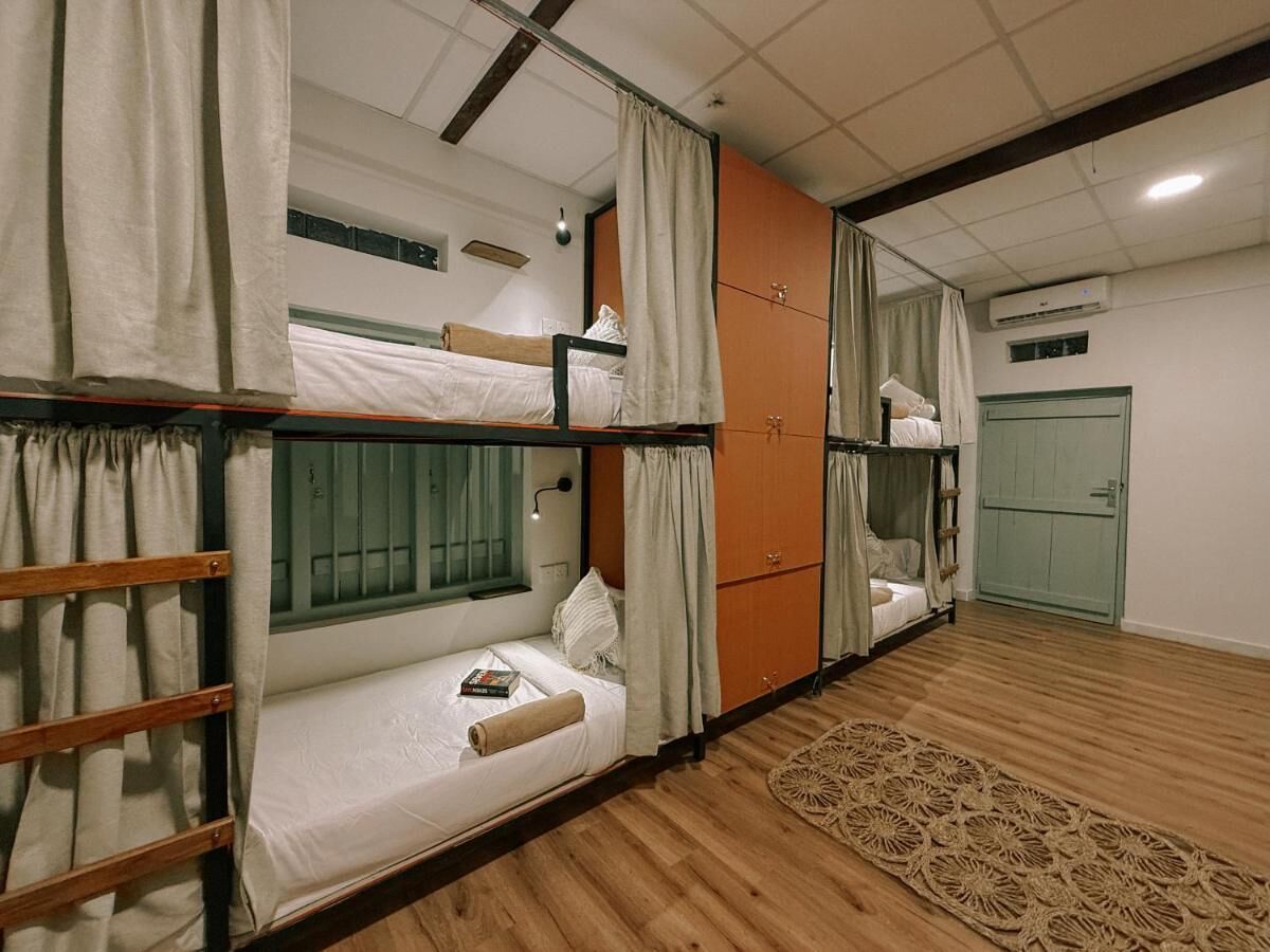 Een slaapzaal met stapelbedden, een klein bureau, een raam met gordijnen en een geweven vloerkleed.