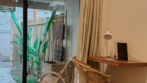 A room with wicker chairs, a laptop on a wooden shelf, and a view of a bamboo fence and plants outside. - Kickin' Surf Lodge (Weligama)