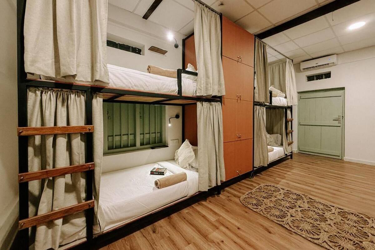 A dormitory-style room with bunk beds, a wooden floor, and a woven rug.