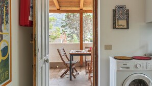 A room with a wooden table and chairs, a washing machine, and a view of the outdoors. - Isola delle Femmine Apartments by Wonderful Italy (Isola delle Femmine)