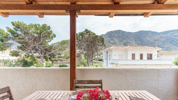 A wooden table with a bowl of flowers, a fish-shaped plate, and a chair on a balcony with a mountain view. - Isola delle Femmine Apartments by Wonderful Italy (Isola delle Femmine)