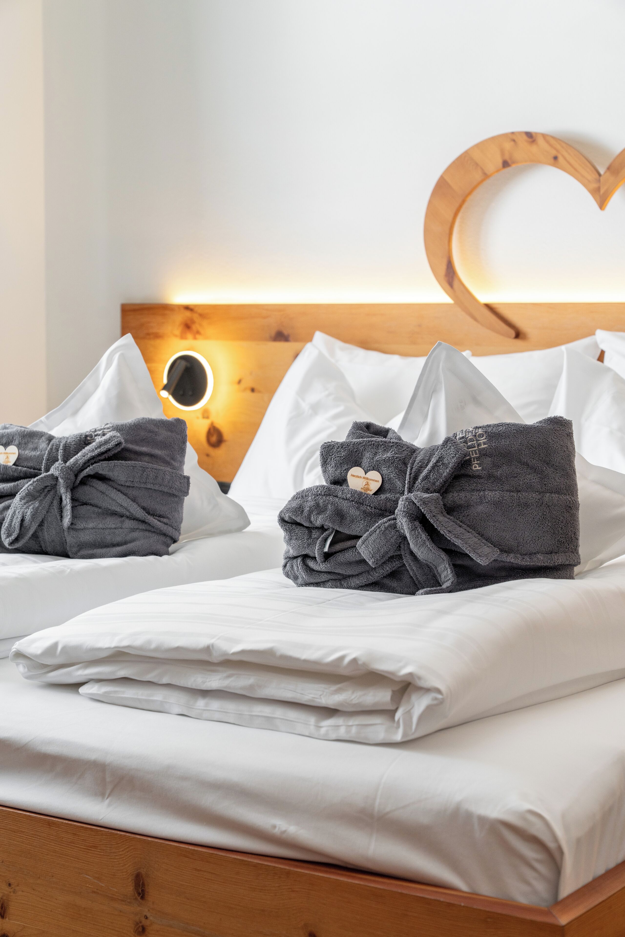 A hotel room with two beds, each with white bedding and gray bathrobes tied with heart-shaped bows.