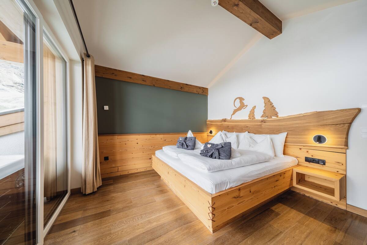 Una cama de madera con ropa de cama blanca, una mesita de noche y una lámpara fijada a la pared.