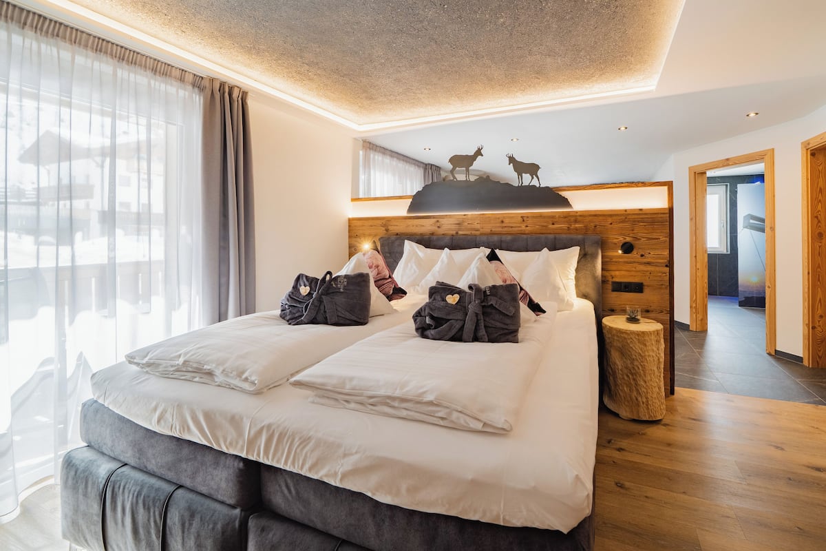 Una habitación de hotel moderna con una cama grande, cabecero de madera y un mural en el techo con ciervos.